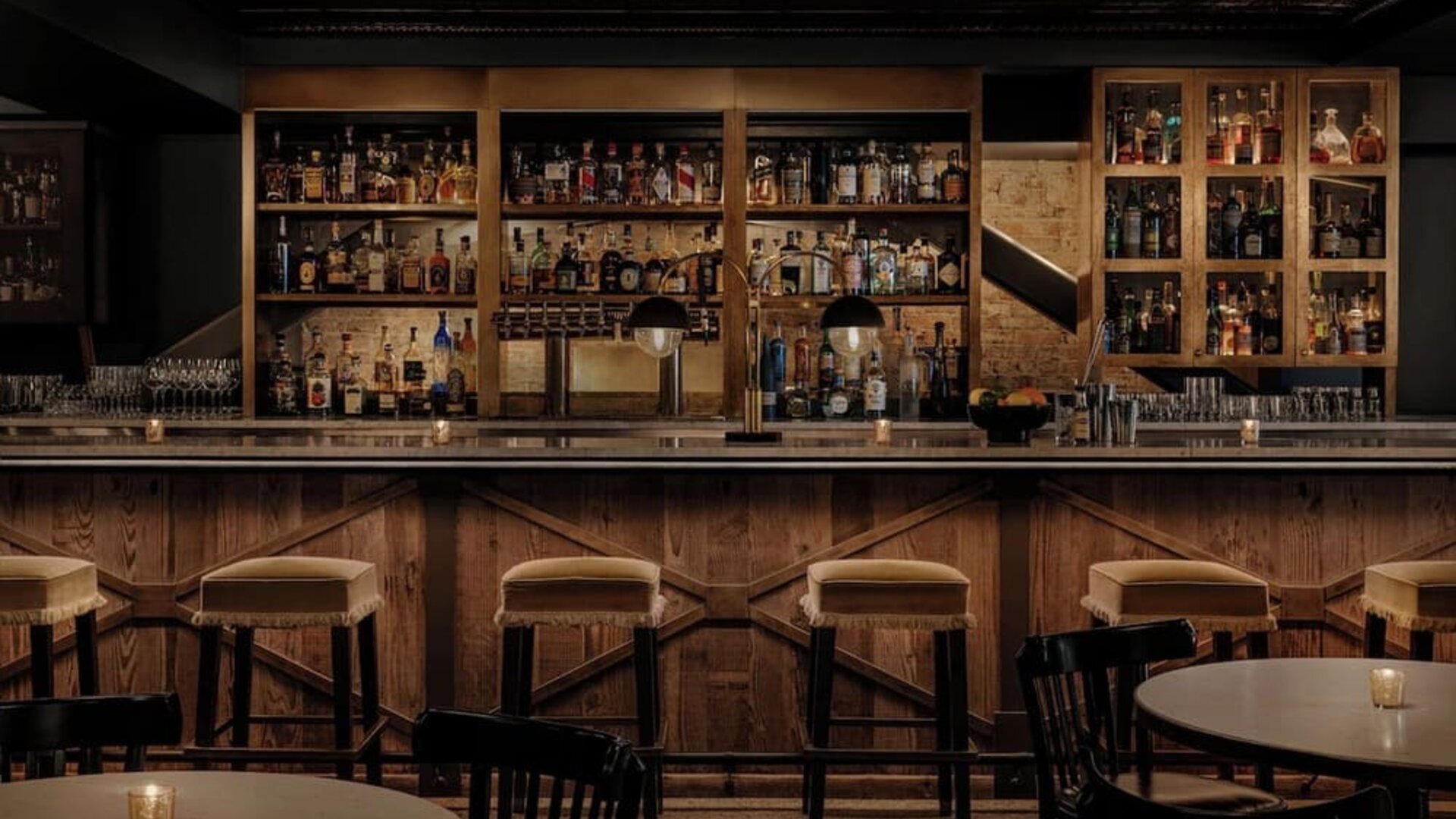 Bar interior with wooden counter, cushioned stools, shelves, and glassware at Kimpton Palladian Hotel.