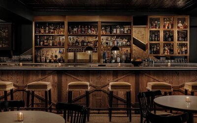 Bar interior with wooden counter, cushioned stools, shelves, and glassware at Kimpton Palladian Hotel.