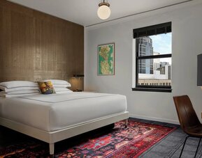 Guest room with king bed, wood accent wall, desk, chair, and patterned rug at Kimpton Palladian Hotel.