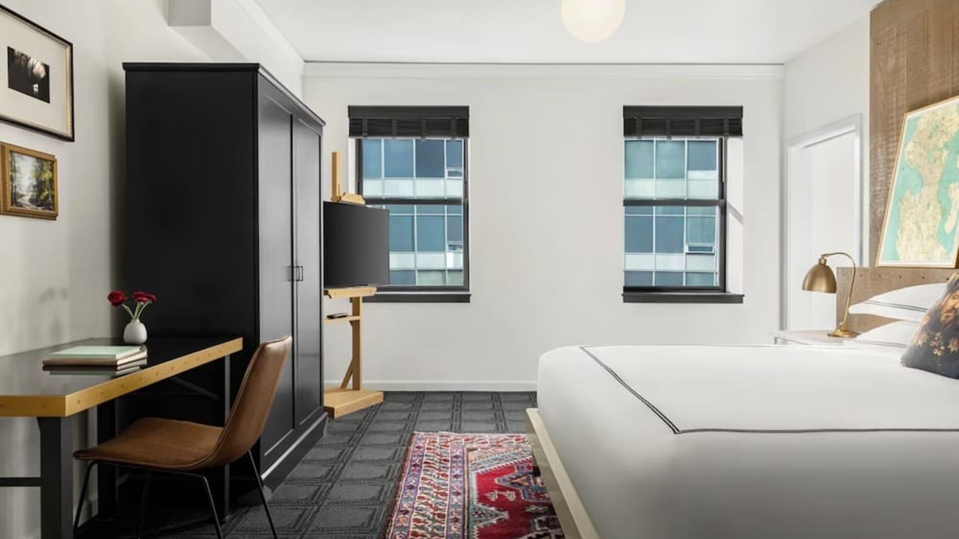 Bedroom workspace with desk, chair, wardrobe, and television beside bed at Kimpton Palladian Hotel.
