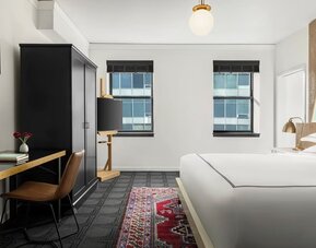 Bedroom workspace with desk, chair, wardrobe, and television beside bed at Kimpton Palladian Hotel.