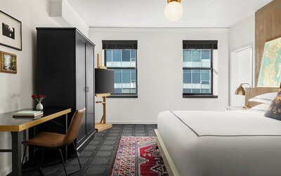 Bedroom workspace with desk, chair, wardrobe, and television beside bed at Kimpton Palladian Hotel.