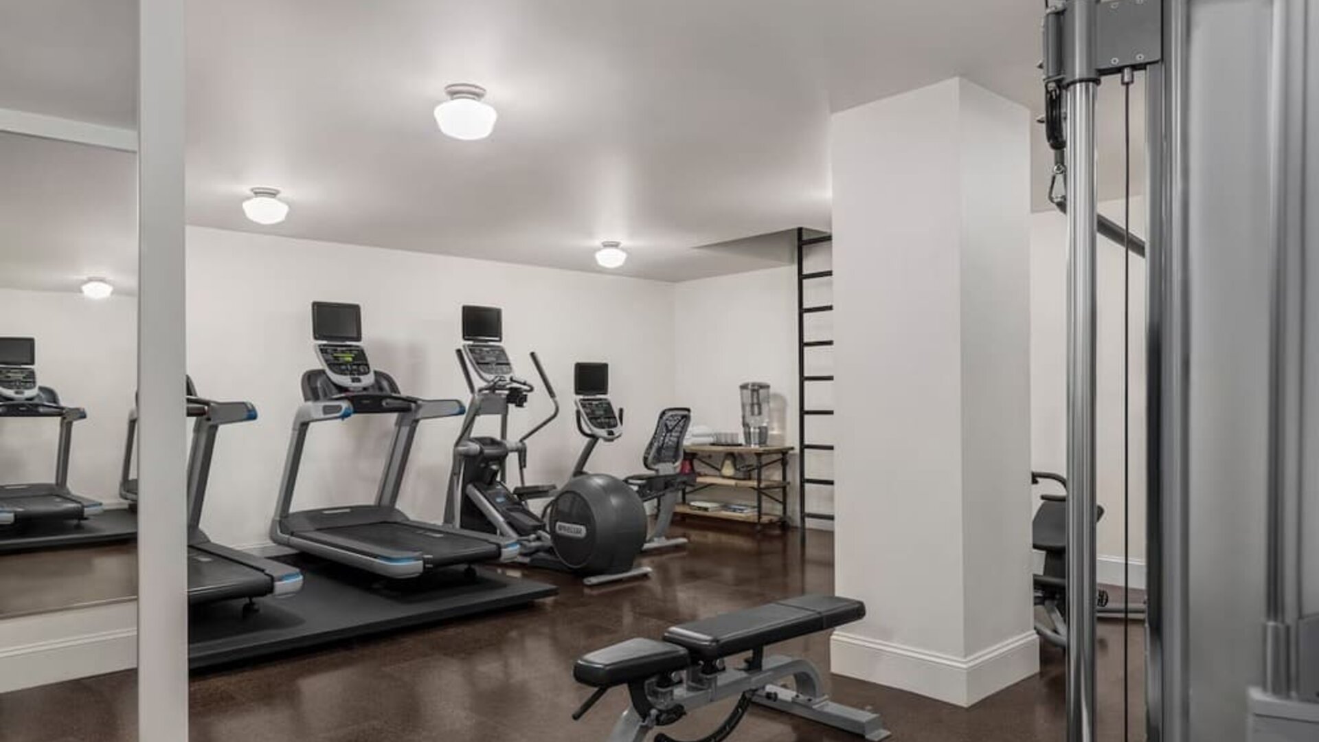 Fitness room with treadmills, weight bench, exercise ball, and mirrored wall at Kimpton Palladian Hotel.
