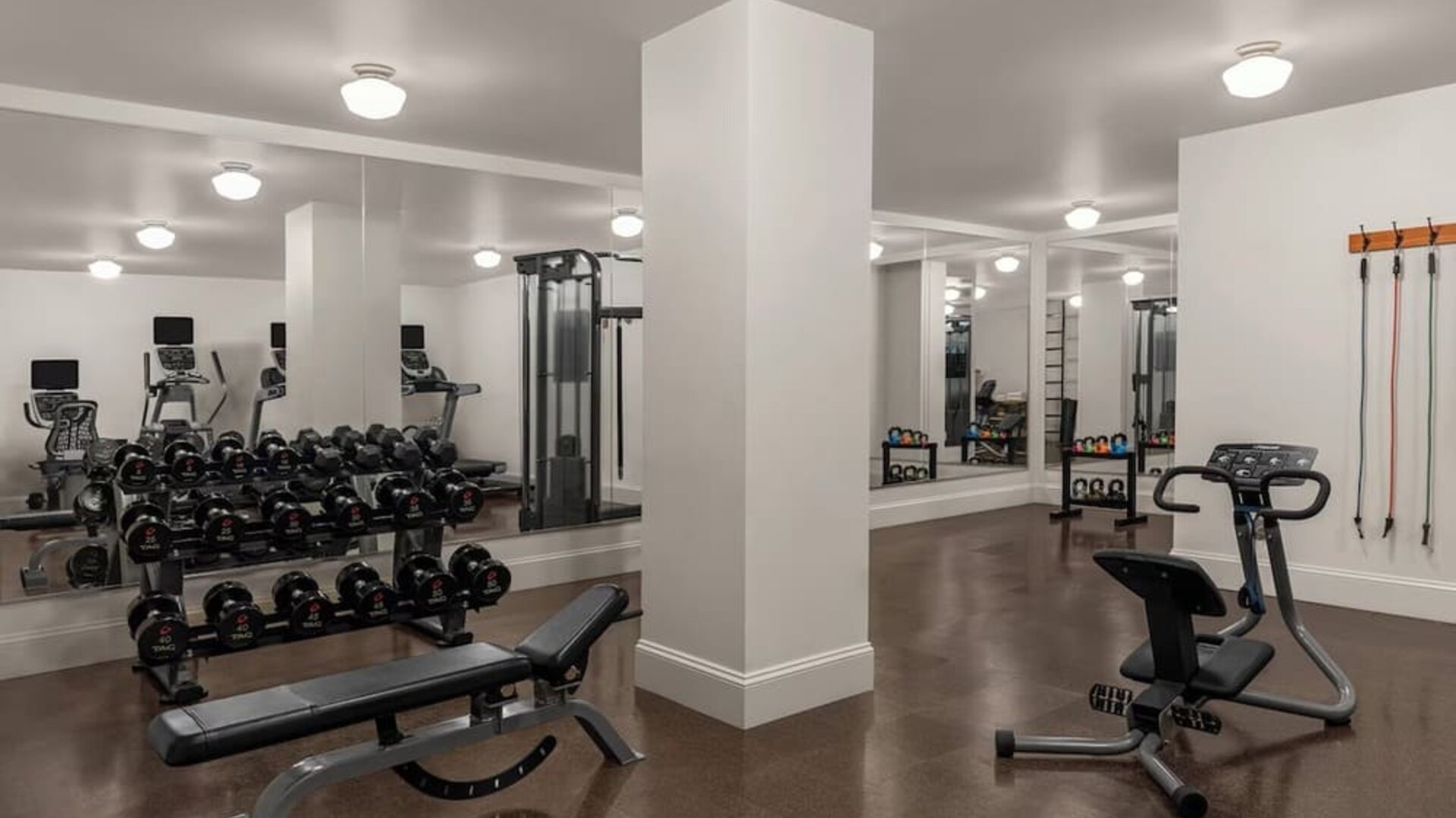 Spacious gym with dumbbells, benches, resistance equipment, and mirrors at Kimpton Palladian Hotel.