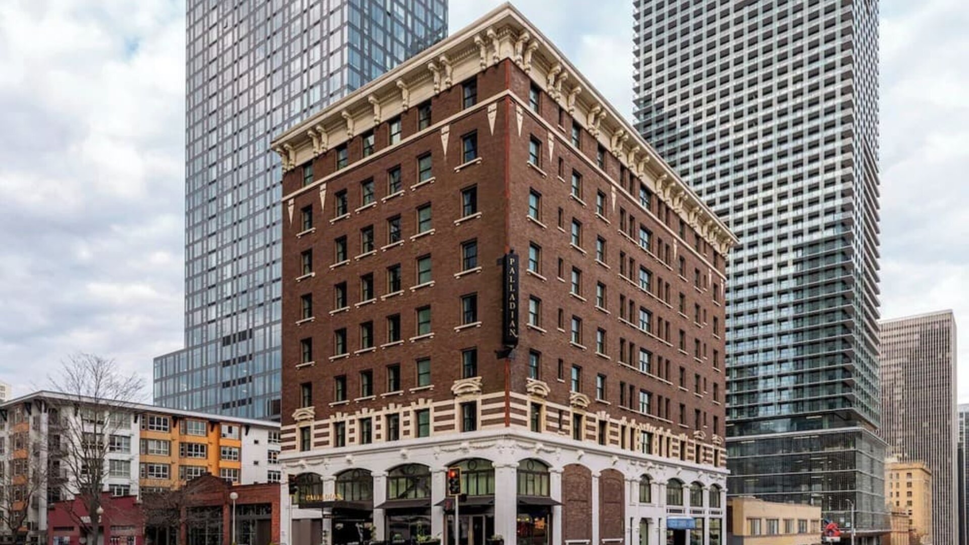 Exterior of multi-story brick building on city corner with surrounding towers at Kimpton Palladian Hotel.