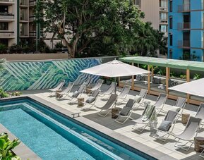 Poolside area with loungers, umbrellas, shaded seating, and bar visible in the background at Romer House Waikiki.