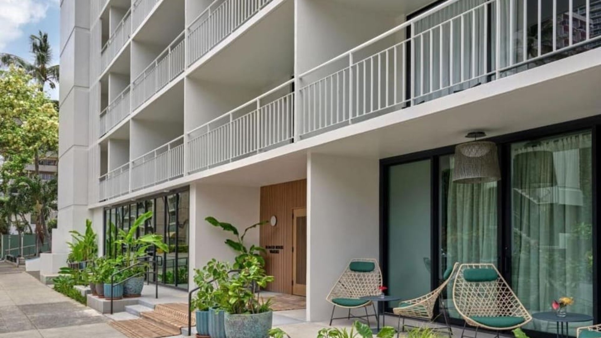 Exterior view of hotel building with balconies, ground-level greenery, and outdoor seating area at Romer House Waikiki.