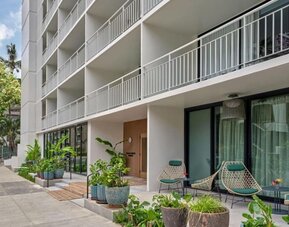 Exterior view of hotel building with balconies, ground-level greenery, and outdoor seating area at Romer House Waikiki.