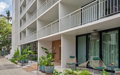 Exterior view of hotel building with balconies, ground-level greenery, and outdoor seating area at Romer House Waikiki.