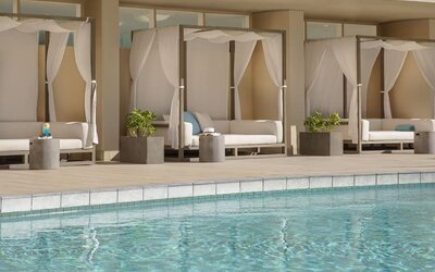 Poolside cabanas with white drapes and cushioned loungers beside outdoor pool at The Twin Fin Hotel.