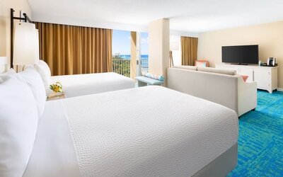 Two double beds with balcony view, seating area, and partial ocean glimpse at The Twin Fin Hotel.
