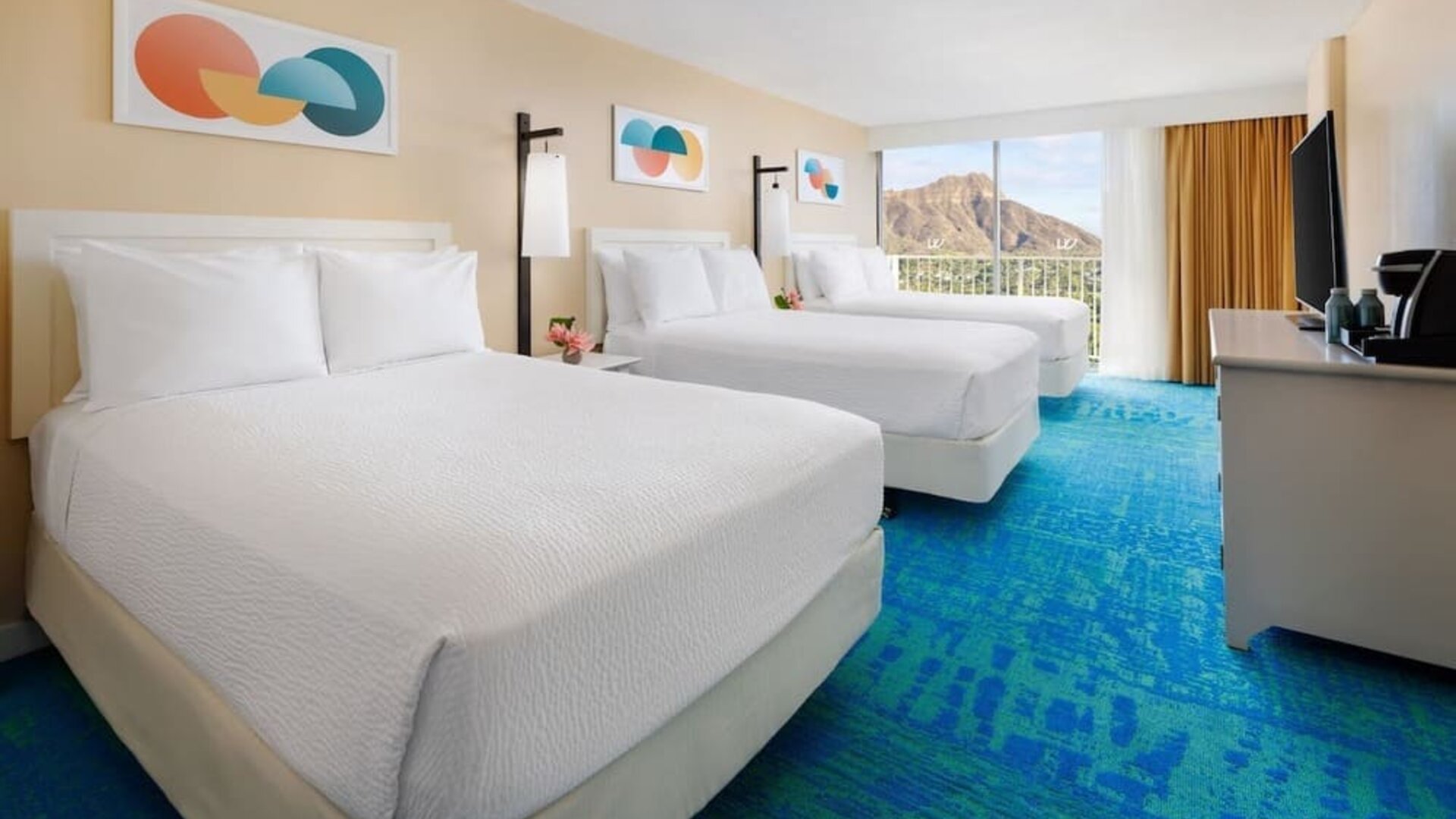 Room with three double beds, balcony view, and mountain backdrop at The Twin Fin Hotel.