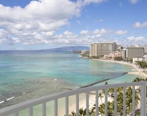 High-rise balcony view overlooking Waikiki Beach, turquoise ocean, and beachfront hotels at The Twin Fin Hotel.