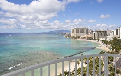 High-rise balcony view overlooking Waikiki Beach, turquoise ocean, and beachfront hotels at The Twin Fin Hotel.