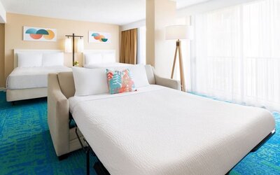 Spacious suite with two beds, sofa bed, and large window with sheer curtains at The Twin Fin Hotel.