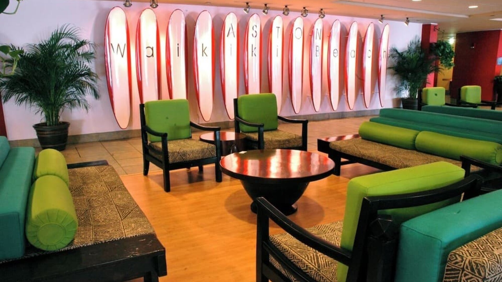 Lobby lounge with green seating and surfboard wall art spelling Waikiki at The Twin Fin Hotel.