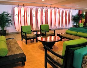 Lobby lounge with green seating and surfboard wall art spelling Waikiki at The Twin Fin Hotel.