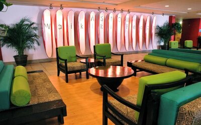 Lobby lounge with green seating and surfboard wall art spelling Waikiki at The Twin Fin Hotel.