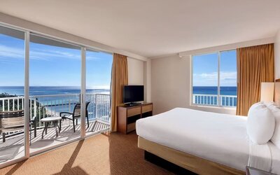 Bright corner room with king bed, large windows, balcony, and sweeping ocean views at Park Shore Waikiki.