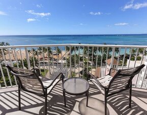 Balcony with two chairs and table overlooking Waikiki Beach, palm trees, and ocean at Park Shore Waikiki.