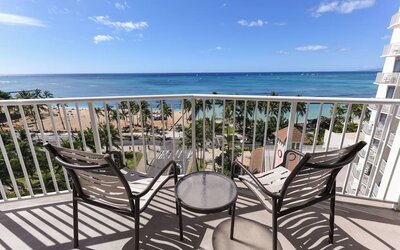 Balcony with two chairs and table overlooking Waikiki Beach, palm trees, and ocean at Park Shore Waikiki.