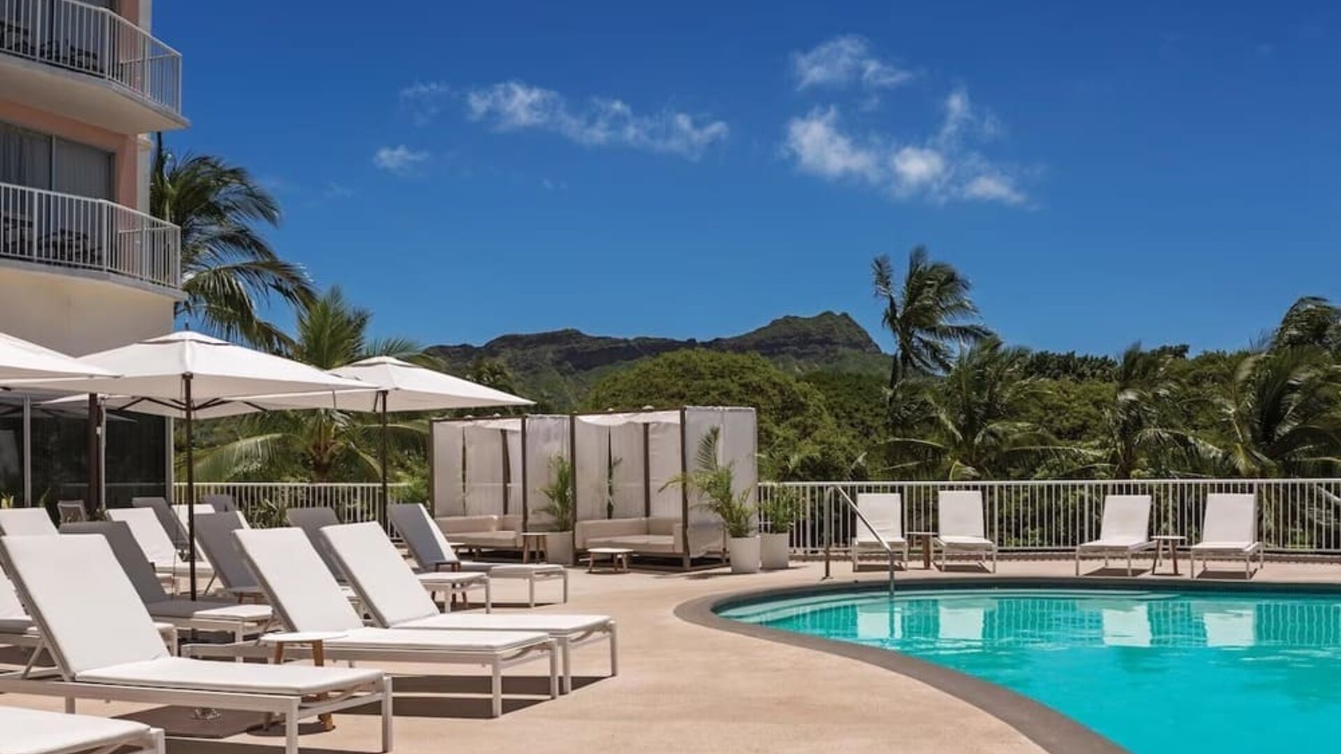 Pool deck with sun loungers, umbrellas, and mountain backdrop at Park Shore Waikiki.
