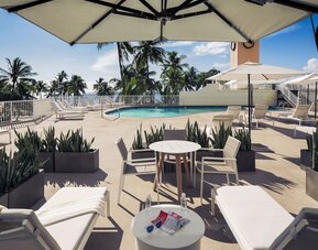 Poolside seating area with tables, loungers, and umbrellas near the outdoor pool at Park Shore Waikiki.