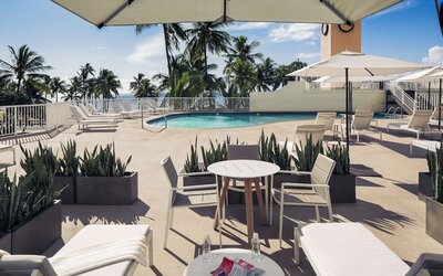 Poolside seating area with tables, loungers, and umbrellas near the outdoor pool at Park Shore Waikiki.