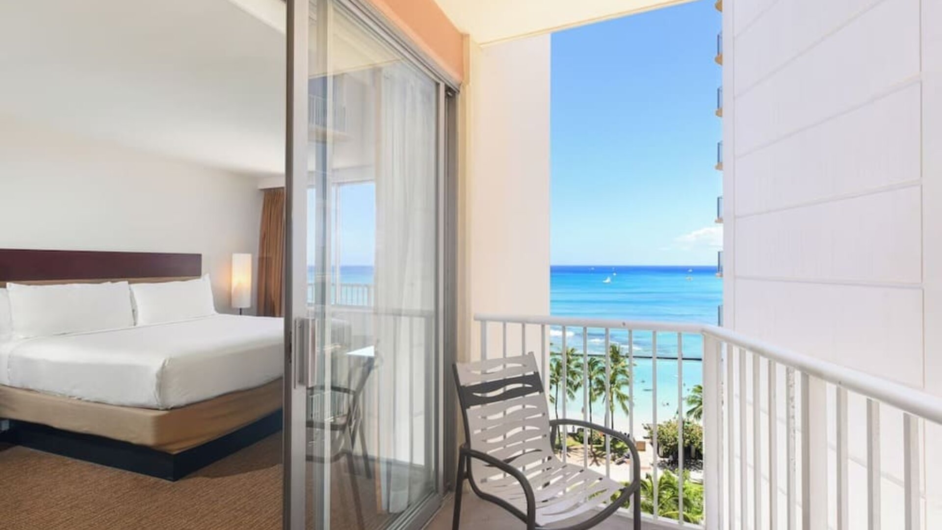 Room with king bed and sliding glass doors leading to a balcony with ocean and pool views at Park Shore Waikiki