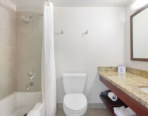 Bathroom with bathtub and shower, granite vanity, mirror, and white tiled walls at Park Shore Waikiki.