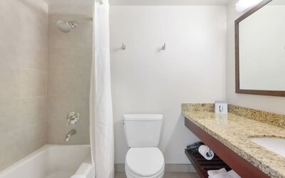 Bathroom with bathtub and shower, granite vanity, mirror, and white tiled walls at Park Shore Waikiki.