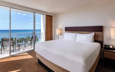 King bed room with ocean-facing balcony, desk, and TV at Park Shore Waikiki.