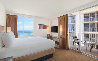 King bed room with balcony view of neighboring buildings and partial ocean view at Park Shore Waikiki.
