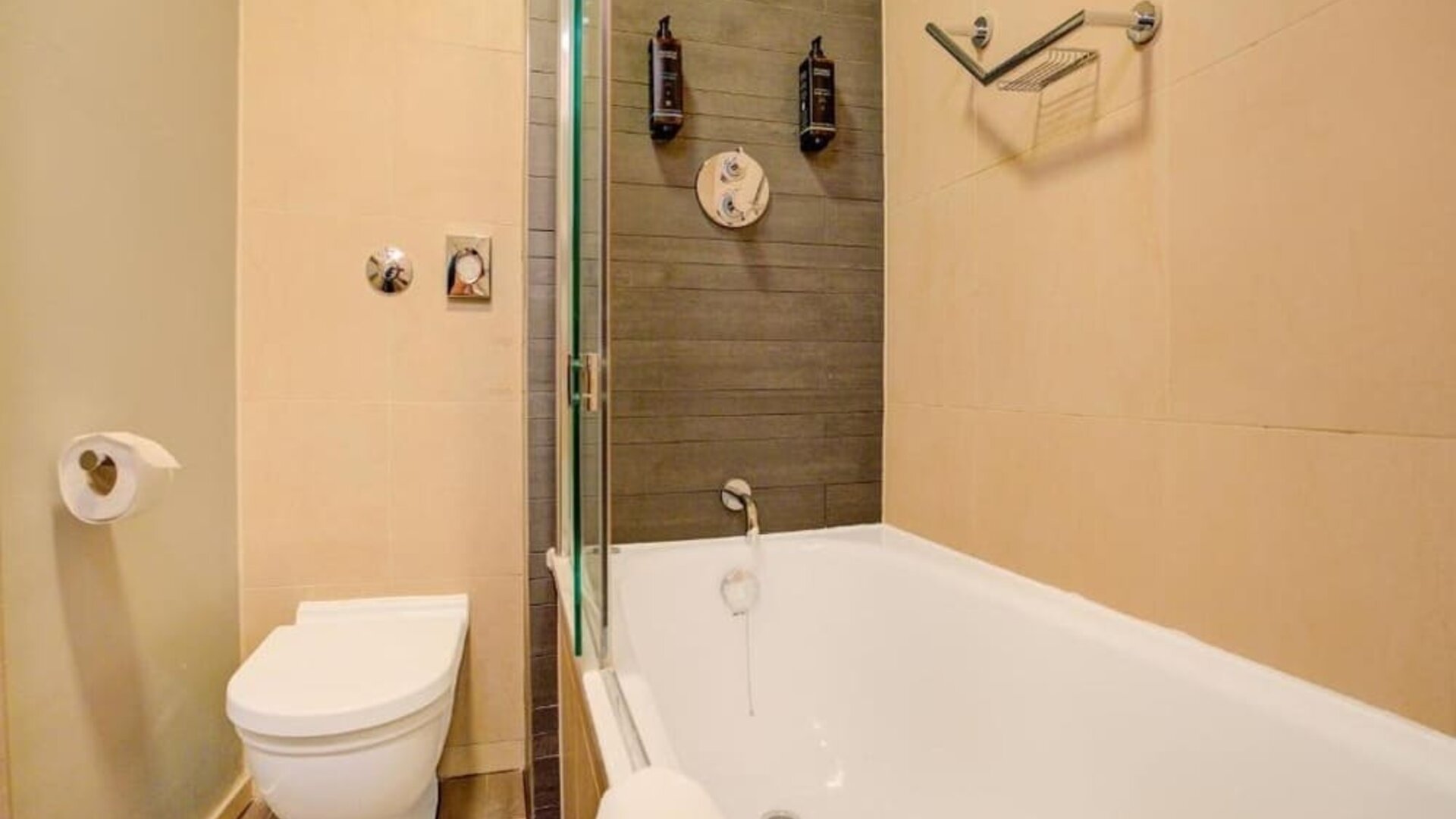 Modern bathroom with bathtub and overhead shower, neutral tiles, and wall-mounted toiletries at Atlantic Tower Hotel Liverpool By Sunday.