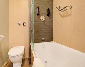 Modern bathroom with bathtub and overhead shower, neutral tiles, and wall-mounted toiletries at Atlantic Tower Hotel Liverpool By Sunday.