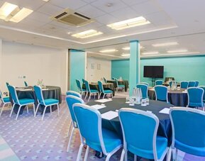 Meeting room with round tables, blue chairs, and presentation screen at Atlantic Tower Hotel Liverpool By Sunday.