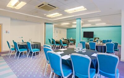 Meeting room with round tables, blue chairs, and presentation screen at Atlantic Tower Hotel Liverpool By Sunday.