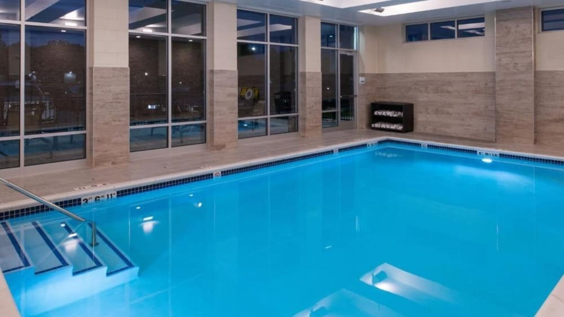 Indoor pool with large windows, entry steps, and poolside seating at Holiday Inn & Suites Farmington Hills - Detroit NW By IHG.
