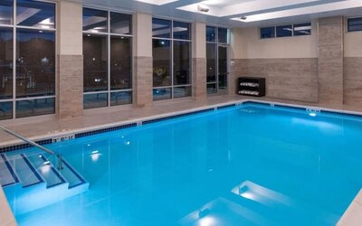 Indoor pool with large windows, entry steps, and poolside seating at Holiday Inn & Suites Farmington Hills - Detroit NW By IHG.