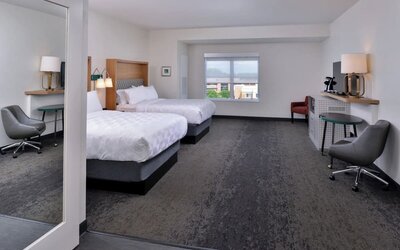 Double queen room with two beds, seating area, desk, and large window at Holiday Inn & Suites Farmington Hills - Detroit NW By IHG.