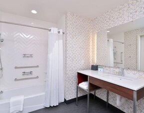 Bathroom with bathtub shower combo, grab bars, patterned wall tiles, and vanity at Holiday Inn & Suites Farmington Hills - Detroit NW By IHG.
