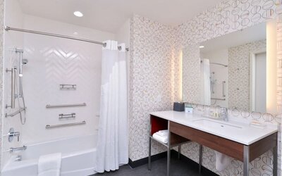 Bathroom with bathtub shower combo, grab bars, patterned wall tiles, and vanity at Holiday Inn & Suites Farmington Hills - Detroit NW By IHG.