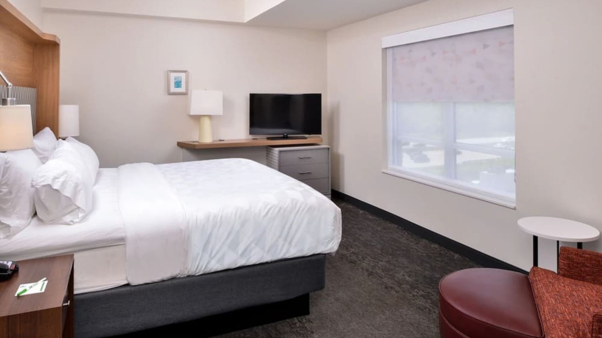 Guest room with large bed, TV, desk area, and window seating at Holiday Inn & Suites Farmington Hills - Detroit NW By IHG.