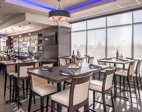 Restaurant dining area with tables, chairs, bar counter, and large windows at Holiday Inn & Suites Farmington Hills - Detroit NW By IHG.