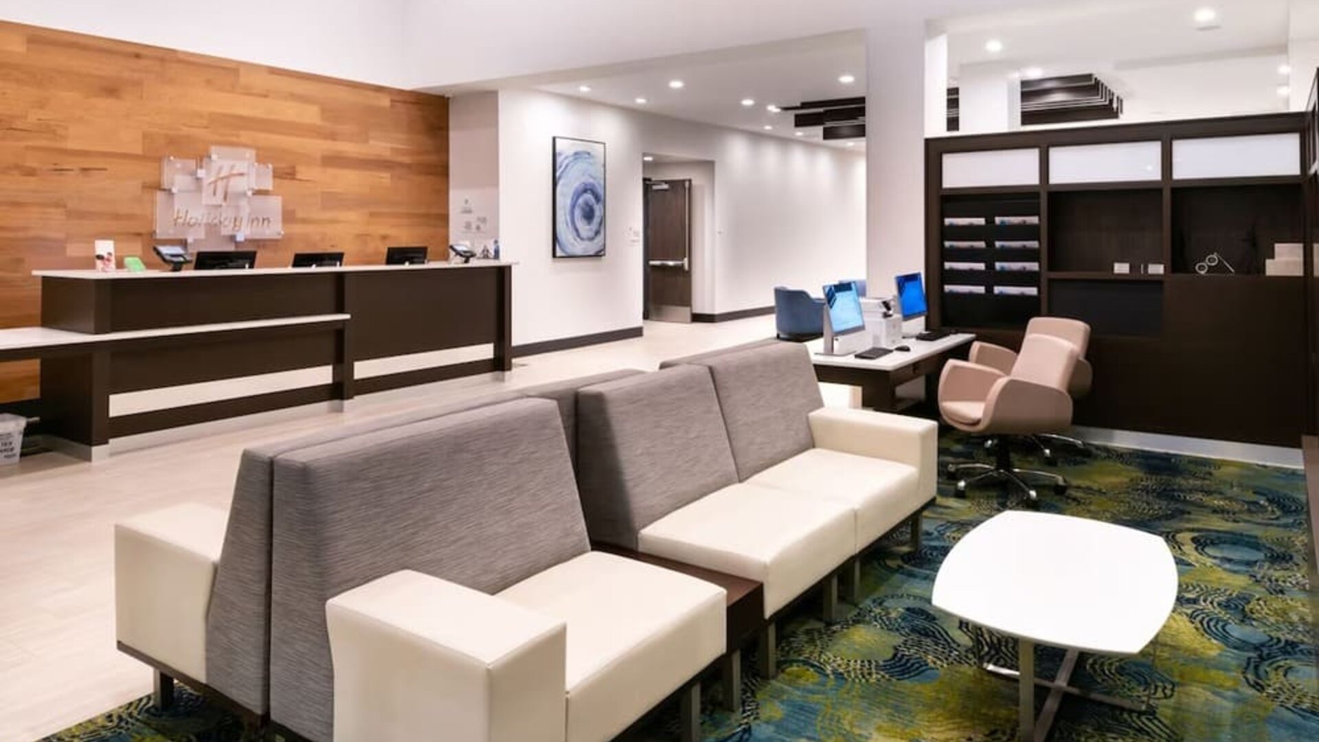 Lobby with front desk, seating area, patterned carpet, and modern decor at Holiday Inn & Suites Farmington Hills - Detroit NW By IHG.