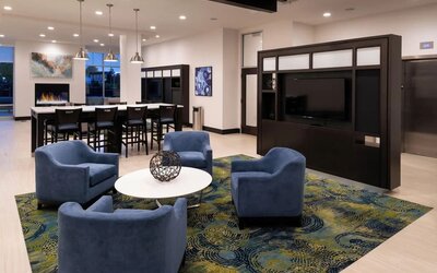 Lounge area with chairs, TV wall, communal table, and fireplace at Holiday Inn & Suites Farmington Hills - Detroit NW By IHG.