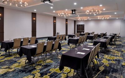 Meeting room with rows of tables, chairs, chandeliers, and patterned carpet at Holiday Inn & Suites Farmington Hills - Detroit NW By IHG.