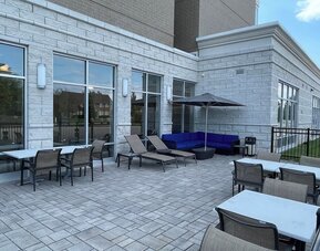 Outdoor patio with lounge chairs, umbrella seating, and paved terrace at Holiday Inn & Suites Farmington Hills - Detroit NW By IHG.