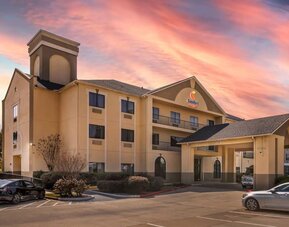 Exterior of hotel building with covered entrance, parked cars, and sunset sky at Comfort Suites Bush Intercontinental Airport.