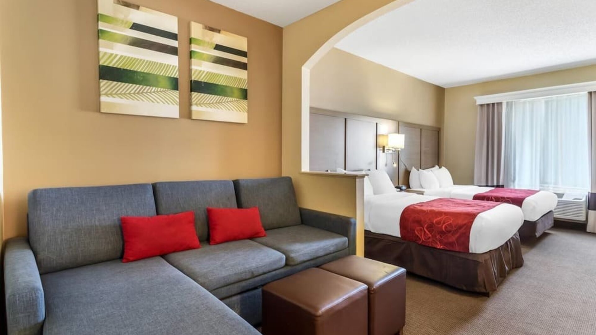 Suite with two beds, sofa seating area, ottomans, and decorative wall art at Comfort Suites Bush Intercontinental Airport.